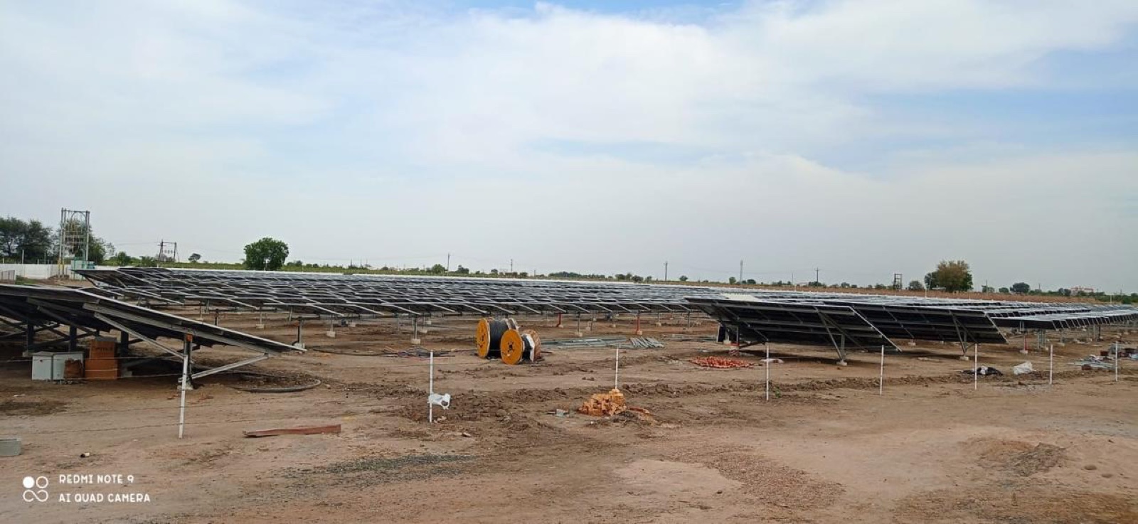 A utility-scale site under construction with partially built module tables and cable drums.