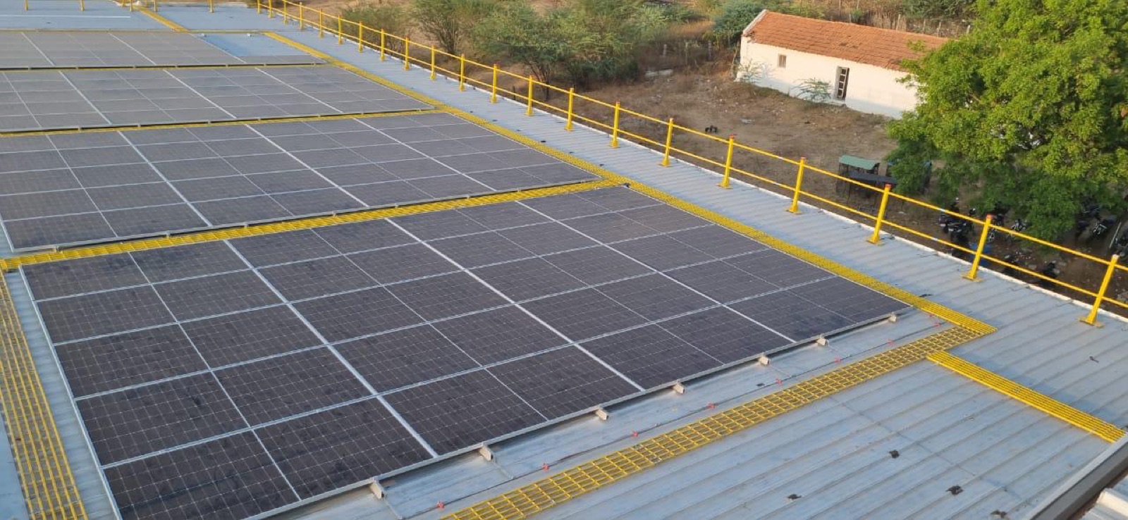 A rooftop solar array with guard-railing along the roof edge and yellow walkways between rows.
